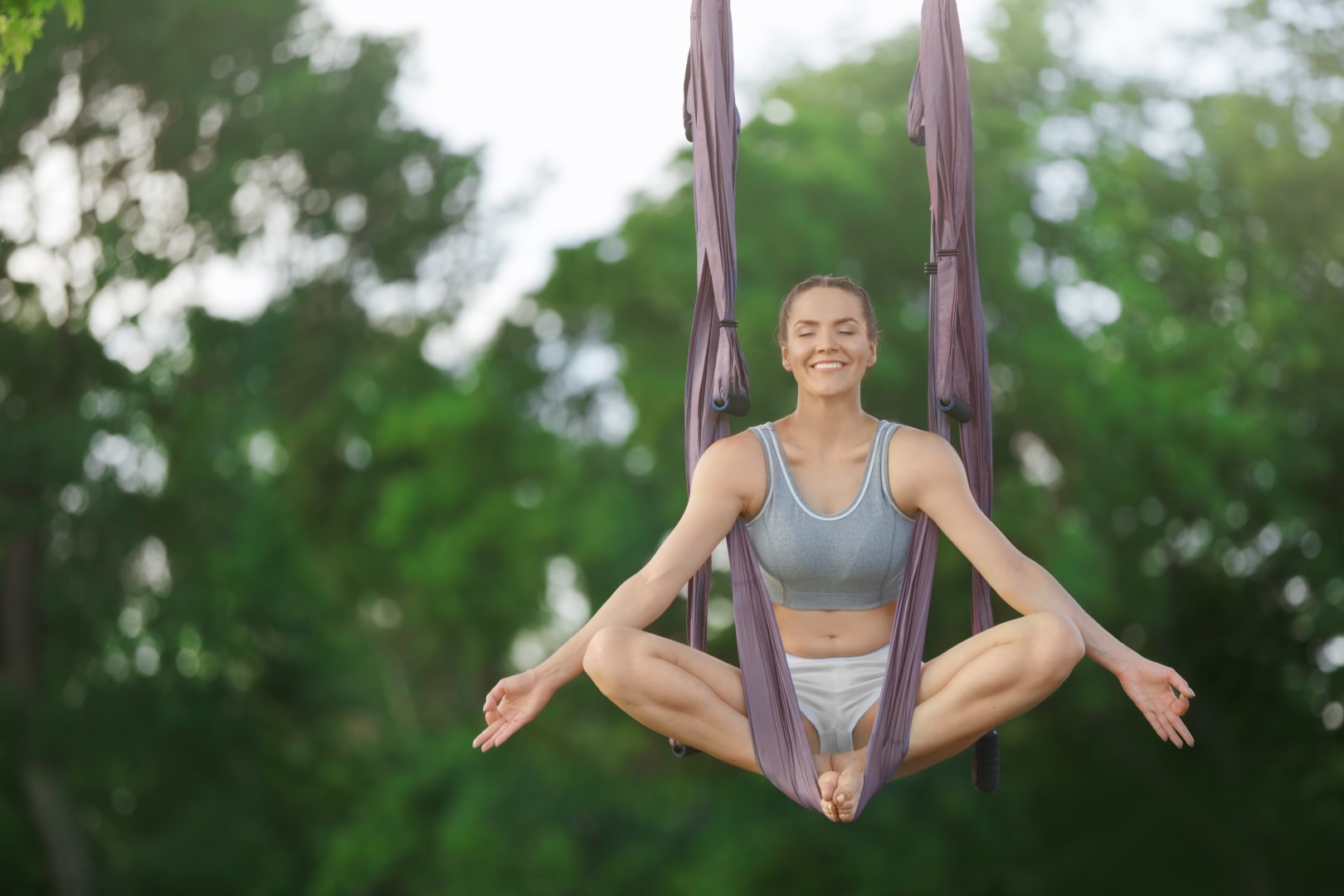 Young woman practicing aerial yoga on tree in park