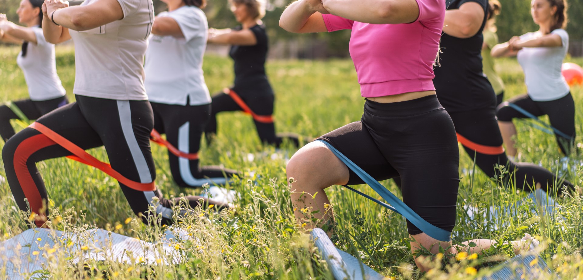 Group of women doing fitness on the grass with rubber bands